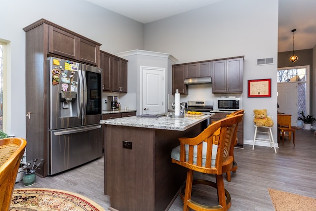 kitchen featuring appliances with stainless steel finishes, decorative light fixtures, dark brown cabinets, and a breakfast bar area