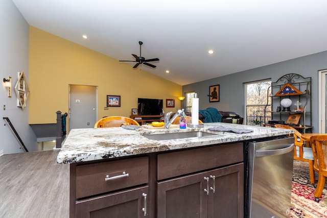 kitchen with sink, vaulted ceiling, light stone countertops, an island with sink, and dark brown cabinets