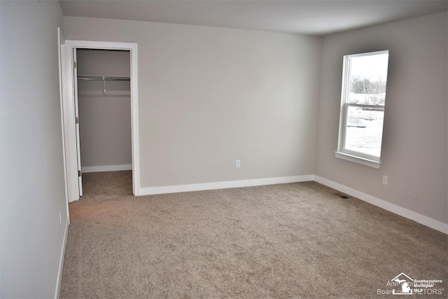 unfurnished bedroom with a spacious closet, a closet, and carpet flooring