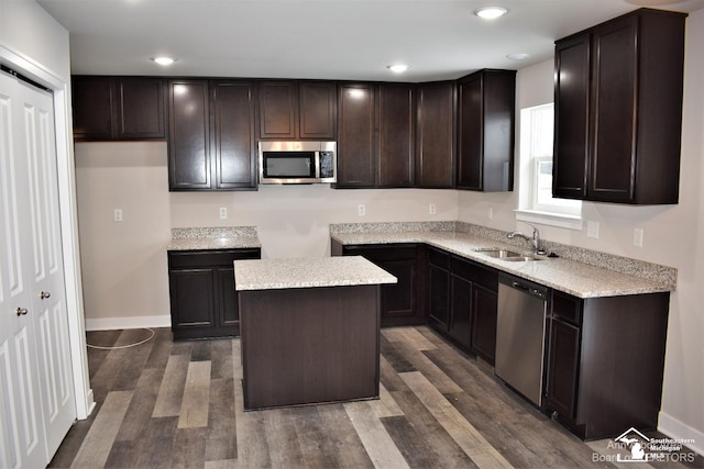 kitchen with appliances with stainless steel finishes, sink, dark brown cabinets, a center island, and dark wood-type flooring