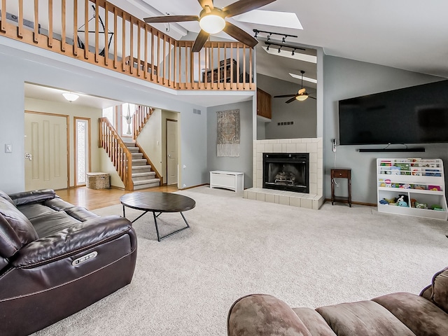 carpeted living room featuring ceiling fan, a tiled fireplace, and high vaulted ceiling