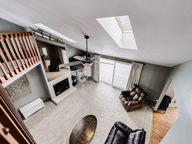 carpeted living room featuring a tile fireplace, rail lighting, a skylight, and ceiling fan