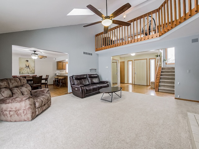 living room featuring high vaulted ceiling, ceiling fan, light carpet, and a skylight