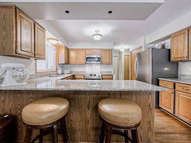 kitchen featuring sink, light hardwood / wood-style flooring, kitchen peninsula, a breakfast bar area, and appliances with stainless steel finishes