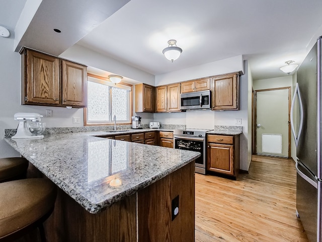 kitchen with sink, light wood-type flooring, kitchen peninsula, light stone countertops, and appliances with stainless steel finishes