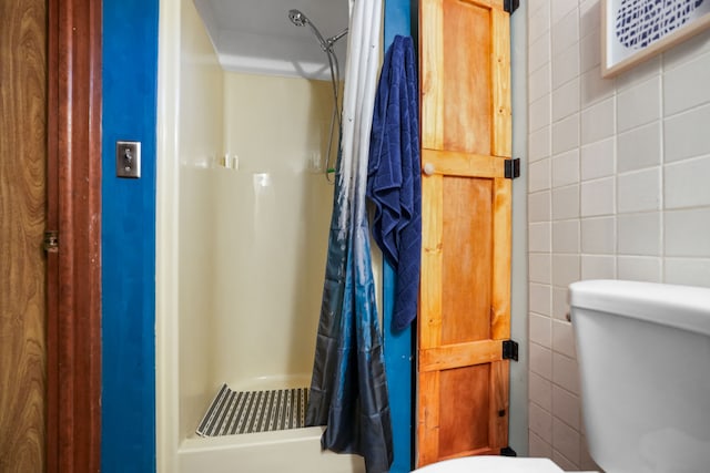 bathroom featuring a shower with curtain, toilet, and tile walls