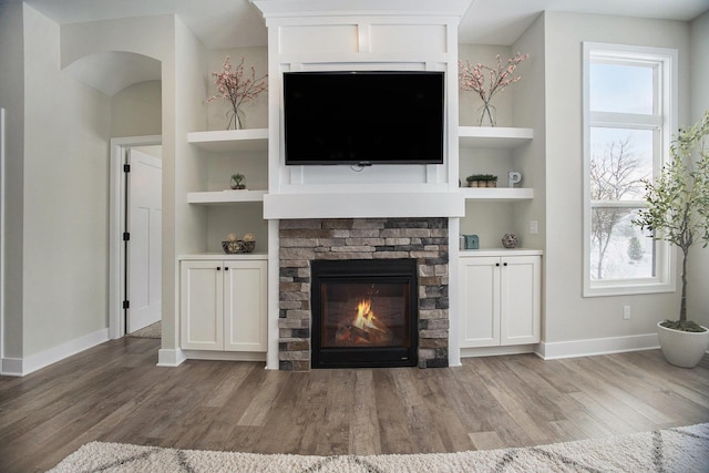 unfurnished living room featuring built in shelves, light hardwood / wood-style floors, and a stone fireplace