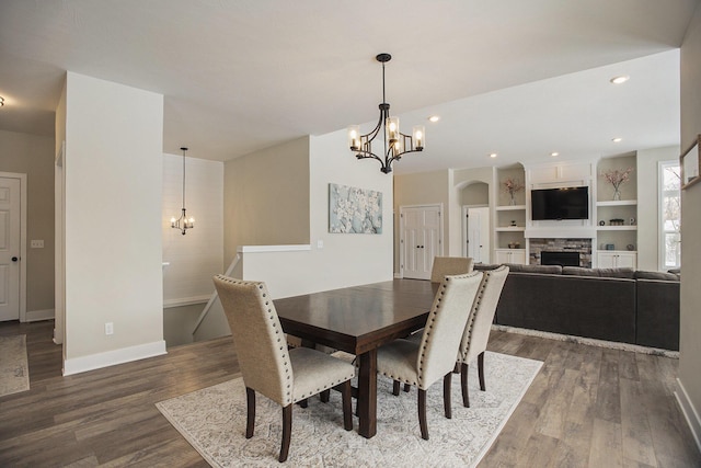 dining space with built in shelves, a fireplace, a chandelier, and dark hardwood / wood-style floors