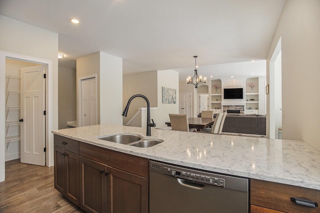 kitchen featuring light stone countertops, stainless steel dishwasher, a fireplace, sink, and a chandelier