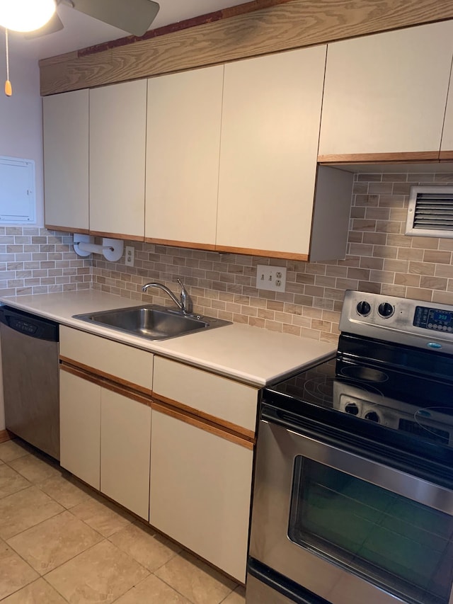 kitchen with appliances with stainless steel finishes, white cabinetry, sink, decorative backsplash, and light tile patterned floors