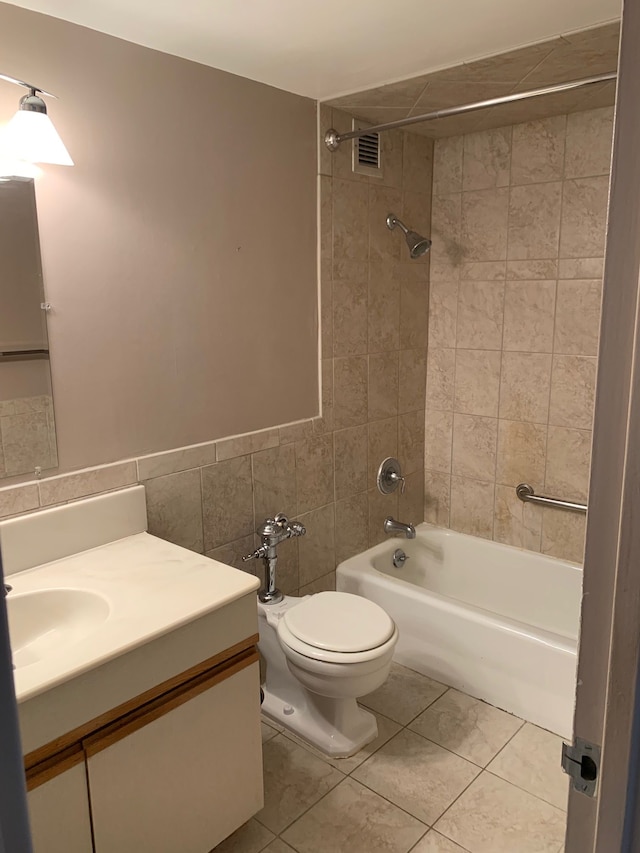 full bathroom with tile walls, tiled shower / bath combo, vanity, toilet, and tile patterned floors