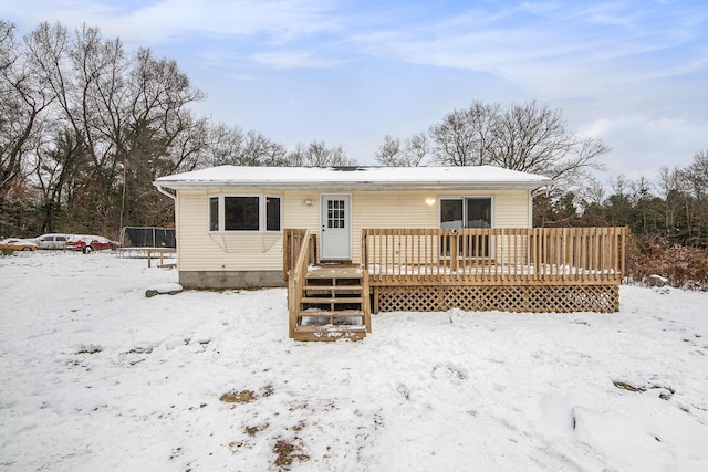 snow covered rear of property with a trampoline and a deck