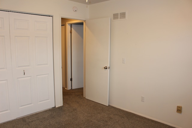 unfurnished bedroom with dark carpet and a closet