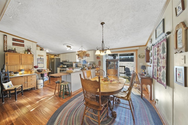 dining space with an inviting chandelier, dark wood-type flooring, a textured ceiling, and ornamental molding