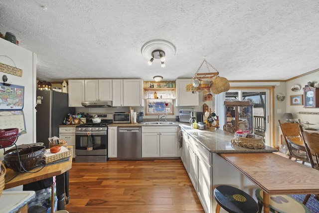 kitchen with white cabinetry, sink, stainless steel appliances, dark stone countertops, and hardwood / wood-style flooring