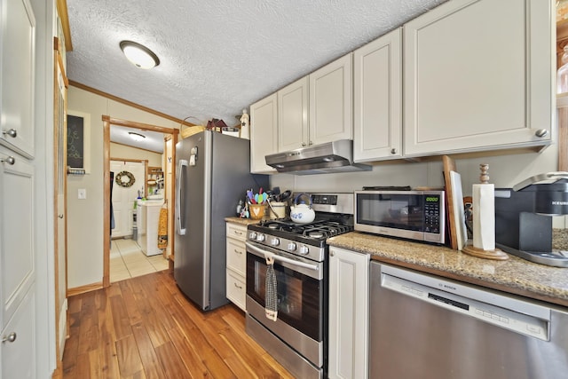 kitchen featuring white cabinets, vaulted ceiling, light wood-type flooring, light stone countertops, and appliances with stainless steel finishes