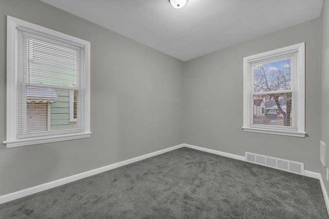 empty room with dark colored carpet and a healthy amount of sunlight