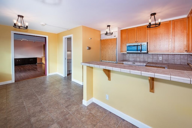 kitchen with tile countertops, hanging light fixtures, tasteful backsplash, kitchen peninsula, and a breakfast bar area