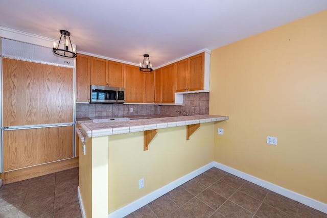 kitchen with decorative backsplash, kitchen peninsula, pendant lighting, tile countertops, and a breakfast bar area