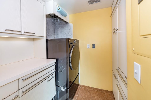 clothes washing area with cabinets, dark tile patterned floors, and washer / clothes dryer