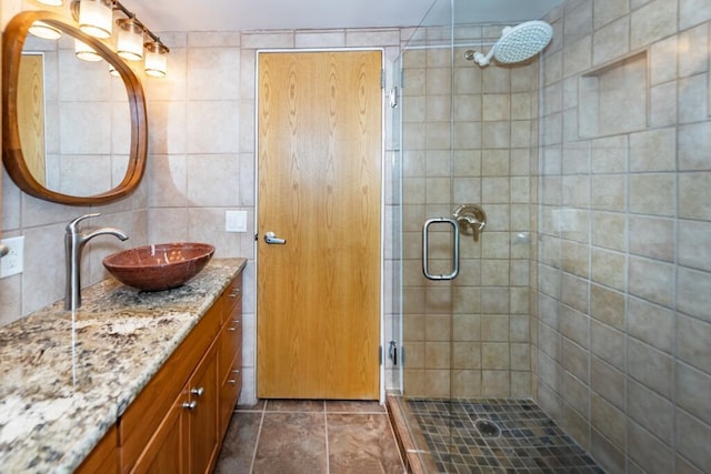 bathroom with tile patterned flooring, vanity, a shower with shower door, and tile walls