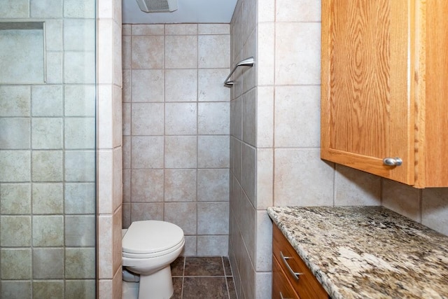 bathroom with vanity, toilet, walk in shower, and tile walls