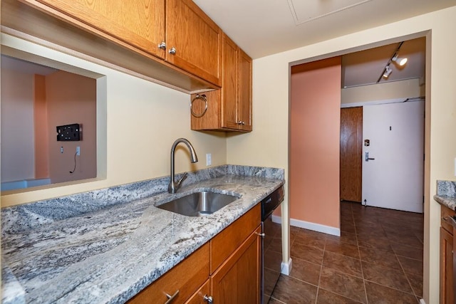 kitchen with dishwasher, track lighting, dark tile patterned flooring, sink, and light stone counters