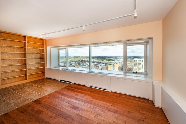 spare room with track lighting, built in features, and hardwood / wood-style flooring