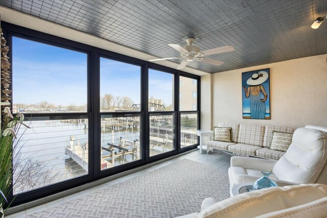 sunroom with ceiling fan and a water view
