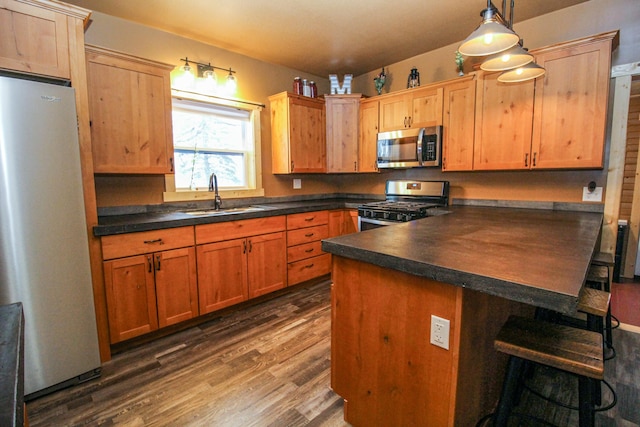 kitchen featuring dark wood-type flooring, a kitchen breakfast bar, sink, appliances with stainless steel finishes, and decorative light fixtures