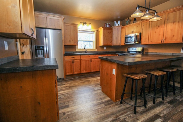 kitchen with appliances with stainless steel finishes, a center island, hanging light fixtures, and dark wood-type flooring