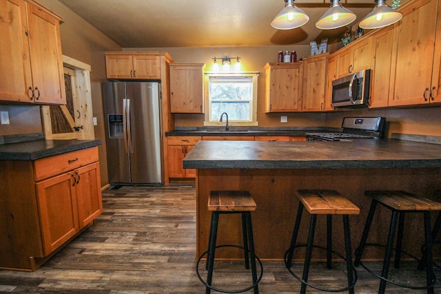 kitchen with dark wood-type flooring, sink, a breakfast bar area, decorative light fixtures, and stainless steel appliances