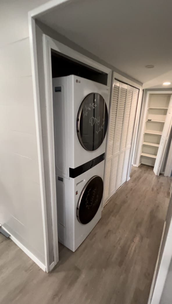 laundry room featuring stacked washing maching and dryer and light hardwood / wood-style floors