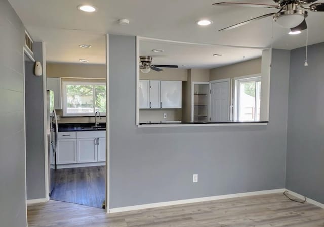 kitchen with a wealth of natural light, white cabinetry, sink, and light hardwood / wood-style floors