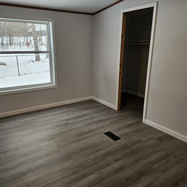 unfurnished bedroom featuring ornamental molding, a walk in closet, dark wood-type flooring, and a closet