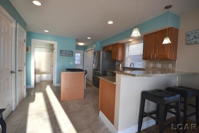 kitchen with a kitchen breakfast bar, hanging light fixtures, tasteful backsplash, light stone counters, and kitchen peninsula