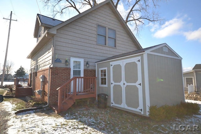 snow covered house featuring a storage shed and a deck