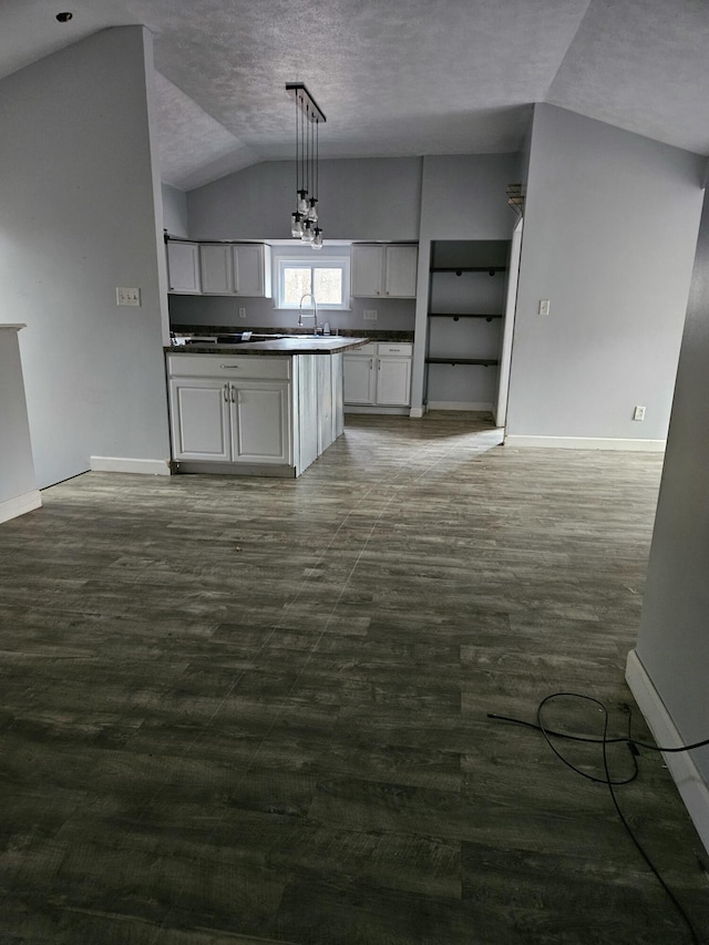 kitchen featuring lofted ceiling, white cabinets, sink, a textured ceiling, and decorative light fixtures