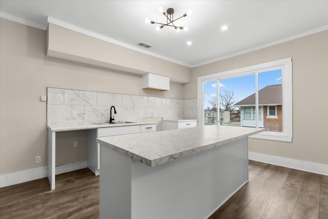 kitchen with tasteful backsplash, dark wood-type flooring, sink, white cabinets, and a center island