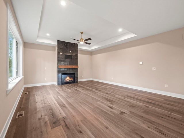 unfurnished living room featuring a tray ceiling, ceiling fan, a high end fireplace, and wood-type flooring