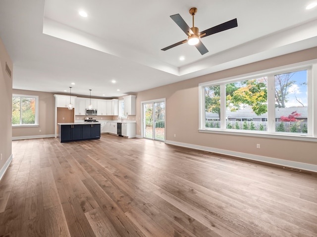 unfurnished living room featuring a raised ceiling, ceiling fan, and hardwood / wood-style floors