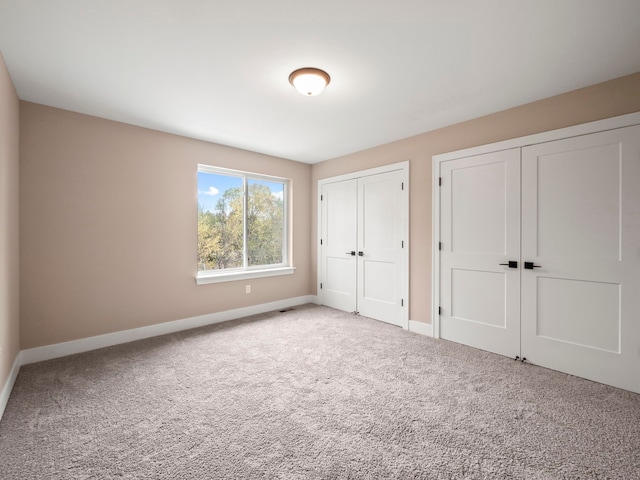 unfurnished bedroom with light colored carpet and two closets