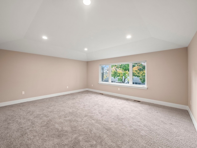 carpeted empty room featuring a raised ceiling and vaulted ceiling