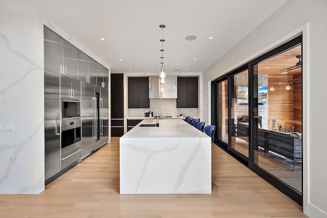 kitchen featuring sink, hanging light fixtures, oven, a kitchen island with sink, and light wood-type flooring