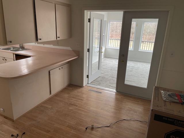 kitchen with french doors, light wood finished floors, light countertops, white cabinetry, and a sink