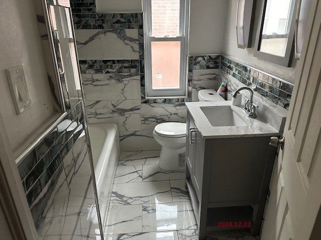 bathroom with a tub to relax in, vanity, tile walls, and toilet