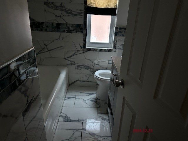 bathroom featuring vanity, a tub to relax in, toilet, and tile walls