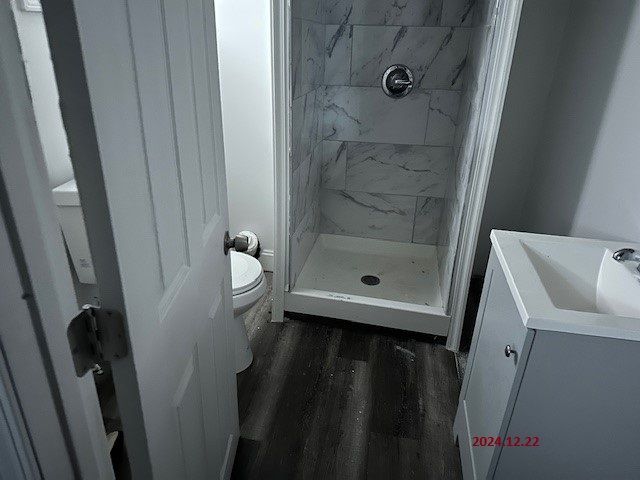 bathroom featuring a tile shower, toilet, vanity, and hardwood / wood-style flooring