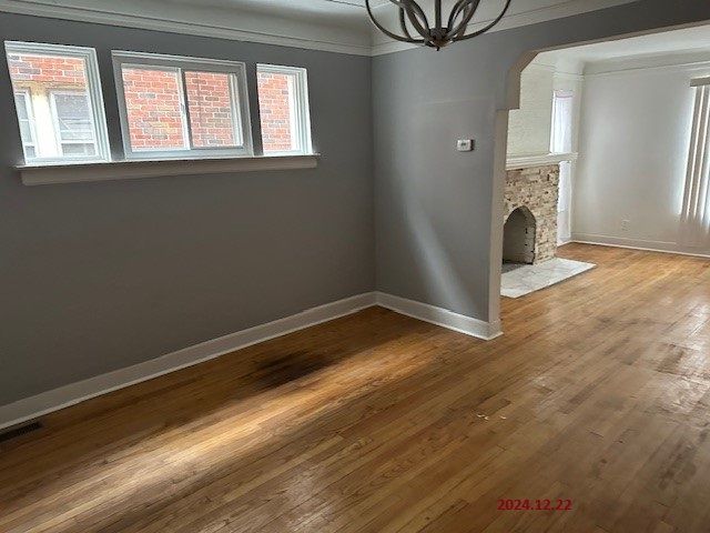 unfurnished living room featuring hardwood / wood-style flooring, a stone fireplace, crown molding, and a chandelier