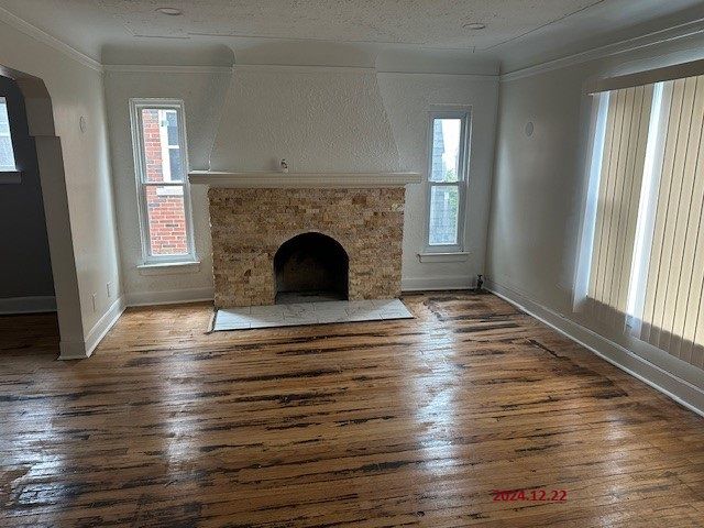 unfurnished living room with a stone fireplace, a wealth of natural light, and crown molding